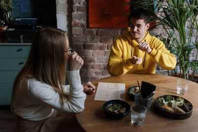 Two people sign to each other across a cafe table over a shared meal.