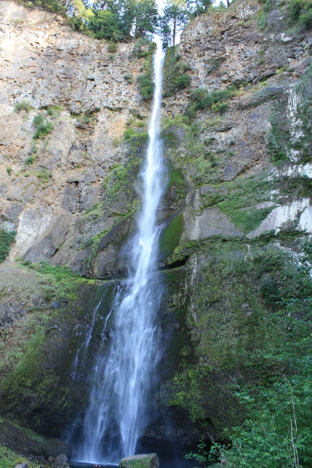 A tall, narrow waterfall streaming down a mossy basalt cliff.
